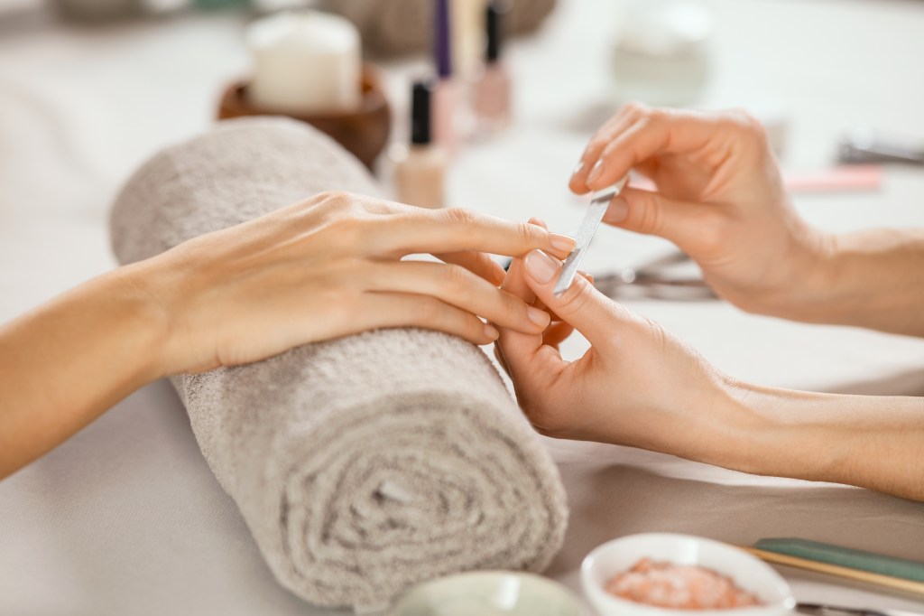 Close-up of a woman getting a manicure in a spa salon, with a beautician using a metal nail file