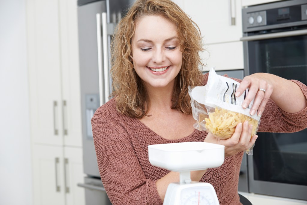 If you are weighing dry food, make sure you note that it is 'uncooked' on your food tracker. Here, a woman pours dried pasta into a scale.