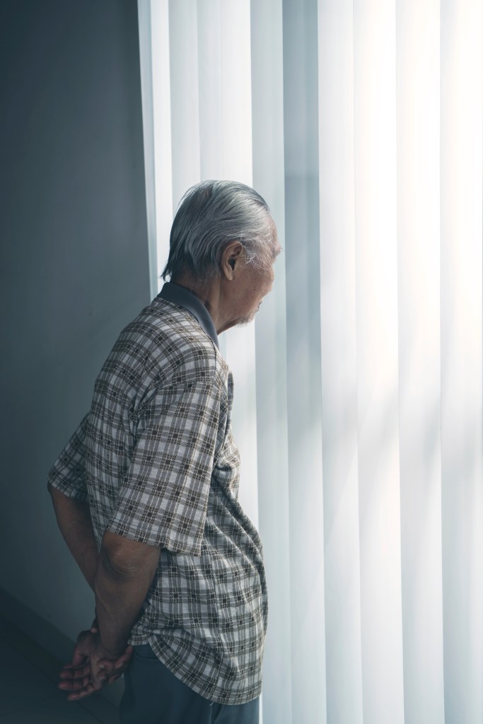 Portrait of a lonely old man looking pensive in a nursing home while standing by the window