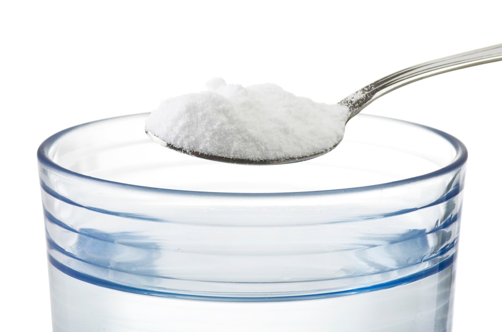 A spoon full of salt hovers over a glass of water