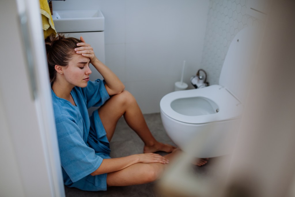 The woman looks nauseous in front of the toilet