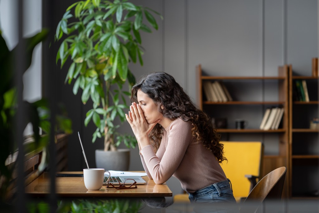 The sad woman sadly feeling tired and worried after reading emails with bad news sitting on the table with the laptop.